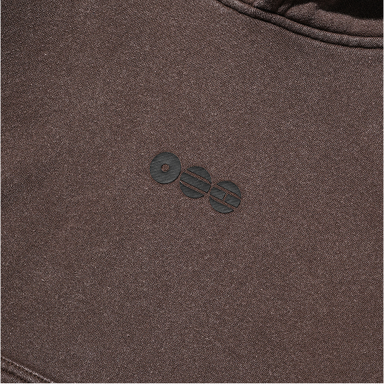Close-up of the small BTS ARIRANG emblem on the brown Tokyo crop hoodie chest.