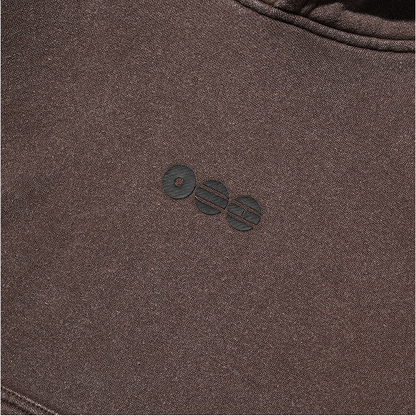 Close-up of the small BTS ARIRANG emblem on the brown Tokyo crop hoodie chest.